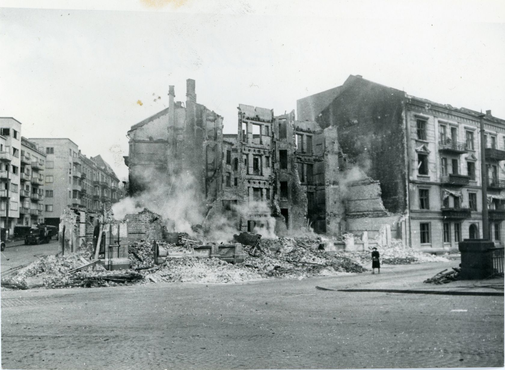 Svart-hvitt foto av en bygning som har blitt bombet. Det er støv opp fra bakken hvor ruinene til bygget falt. 
