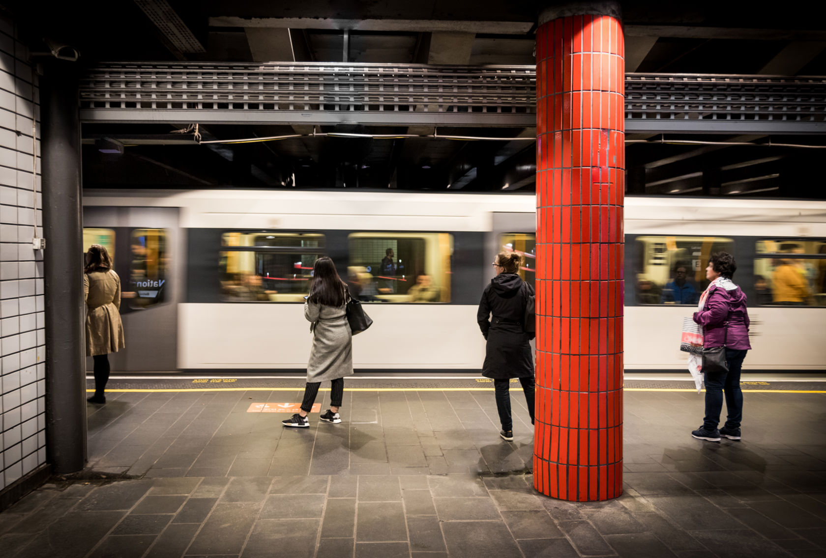 Reisende på plattformen ved Nationaltheatret T-banestasjon mens et T-banetog passerer.