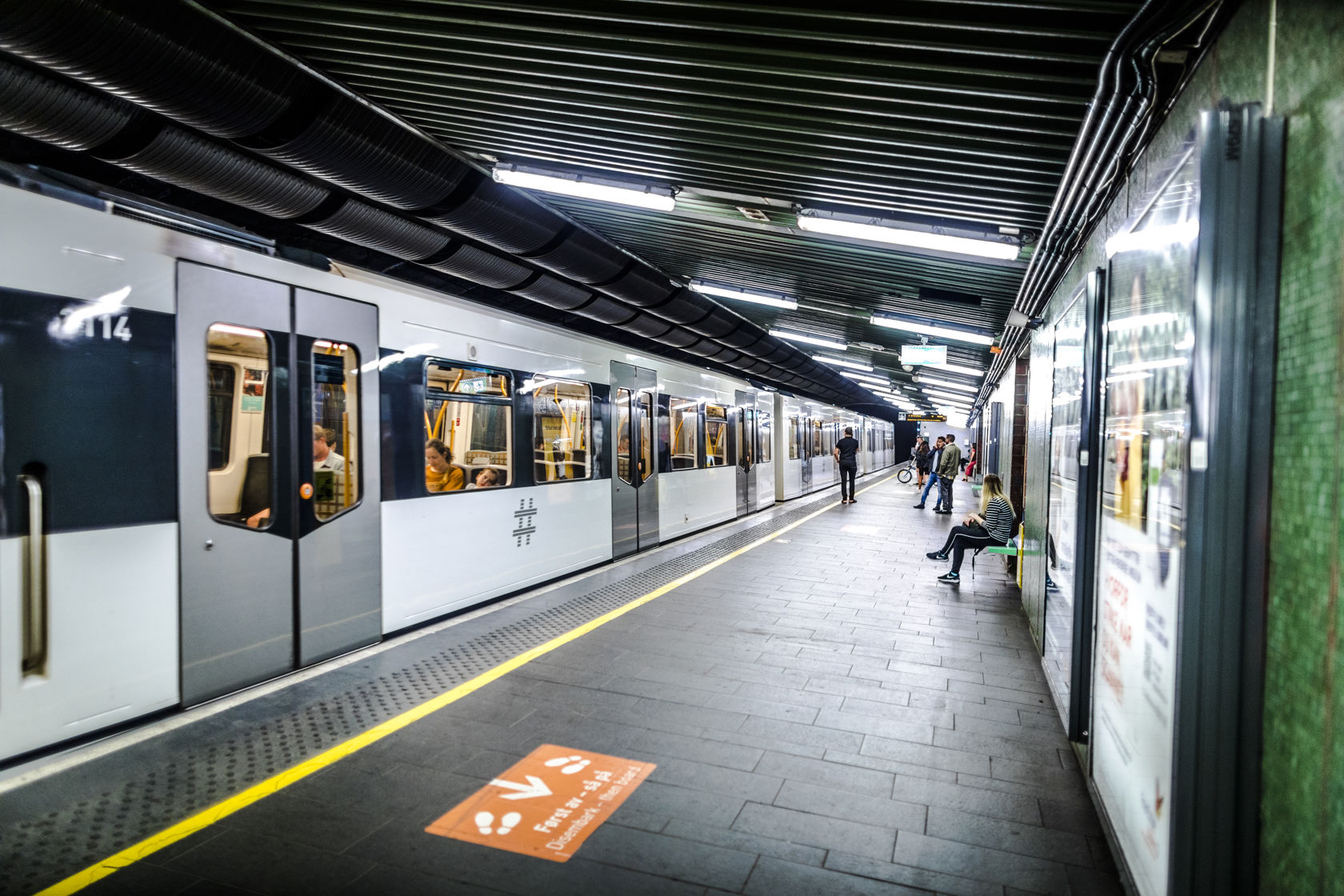 T-banetog ved plattformen på Tøyen T-banestasjon med ventende reisende.